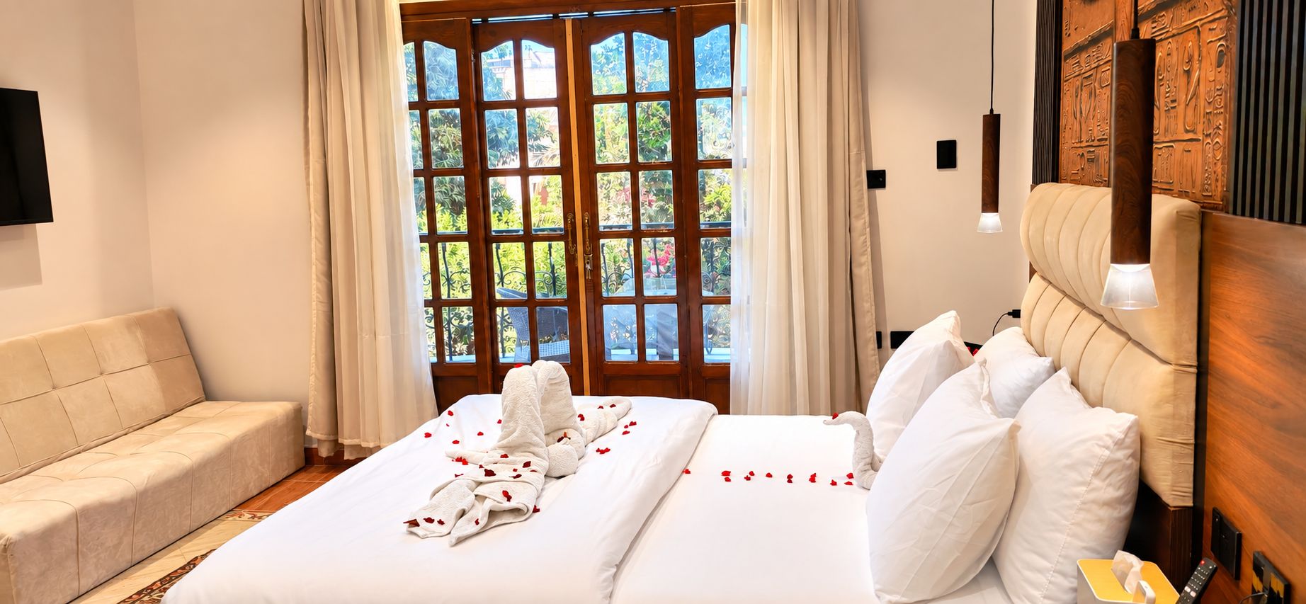 Habitación de hotel con cama, sofá, cabecero de madera y vistas a través de un ventanal grande.