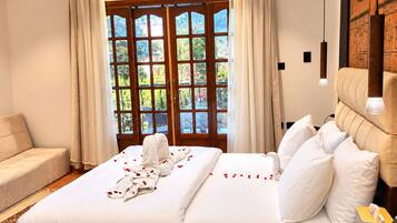 Habitación de hotel con cama, sofá, cabecero de madera y vistas a través de un ventanal grande.