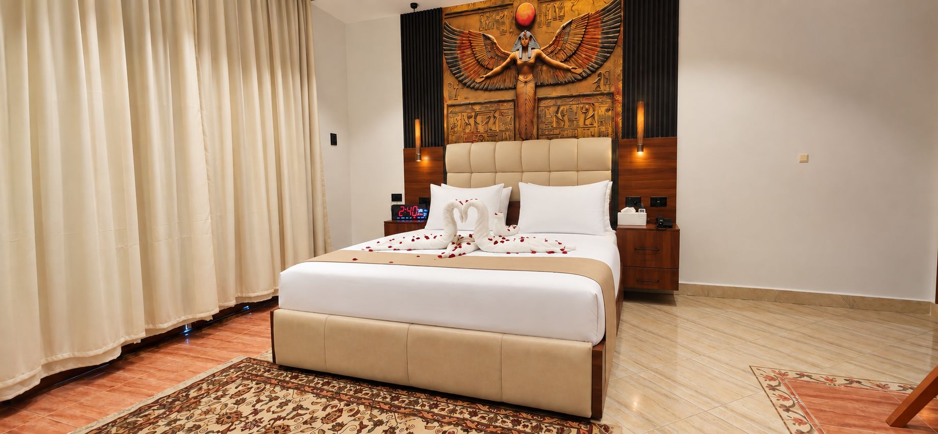 Une chambre d’hôtel avec un grand lit, une tête de lit en bois, une fresque murale et une table de chevet avec une lampe.