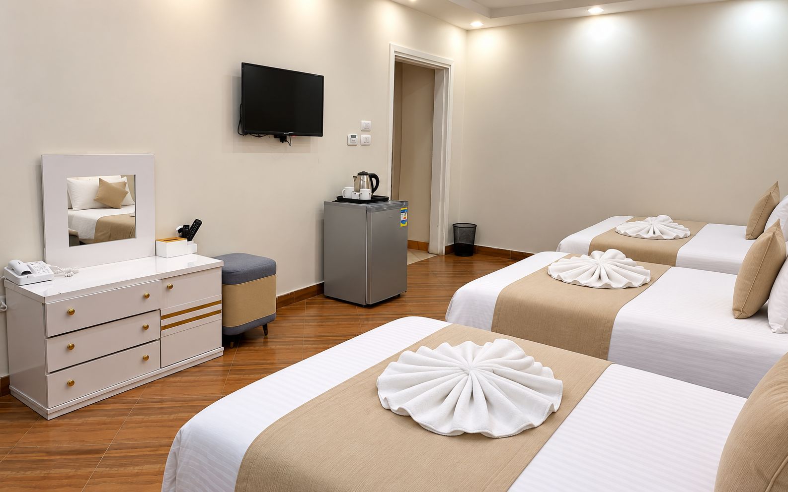 A hotel room with two beds, a TV, a minibar, and a desk with a telephone.