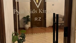 A hallway with a wooden door labeled "Pyramid Kingdoms RZ" and a potted plant. - Pyramids Kingdom RZ Hotel  (Giza)