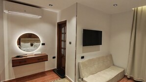 A bedroom with a bed, a bedside table, a mirror, a TV mounted on the wall, and a window with curtains. - Pyramids Kingdom RZ Hotel  (Giza)