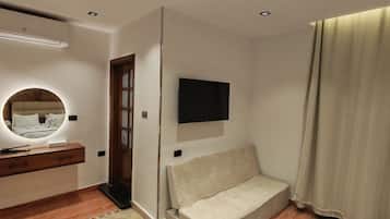 A bedroom with a bed, a bedside table, a mirror, a TV mounted on the wall, and a window with curtains.