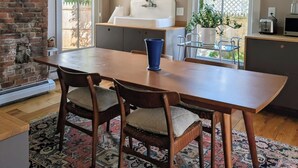 A kitchen with a brick wall, a large window, a sink, and a dining area with chairs and a table. - Chic 3-bedroom house in Munjoy Hill with off-street parking.   (Portland)