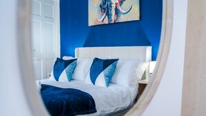 Un lit avec une literie blanche et bleue, une tête de lit blanche et un mur bleu orné d’un tableau.