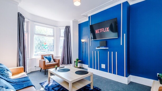 Un salon moderne avec un mur d’accent bleu, un téléviseur à écran plat, un canapé, une table basse et une fenêtre avec des rideaux.