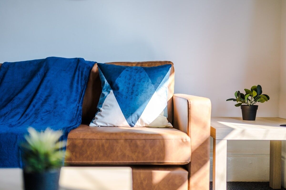 A room with a brown leather sofa, a blue and white pillow, a small potted plant, and a wooden table.