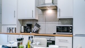 Une cuisine moderne avec des armoires blanches, une hotte en acier inoxydable, un four à micro-ondes et un coin repas comprenant une table, des chaises et une petite plante en pot.