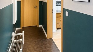 Um corredor com porta de madeira, radiador branco e um quadro na parede.