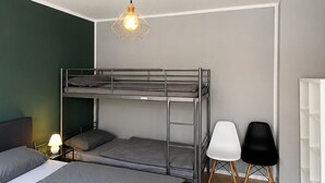 Um quarto com beliches, uma escrivaninha, duas cadeiras, um abajur e um lustre.