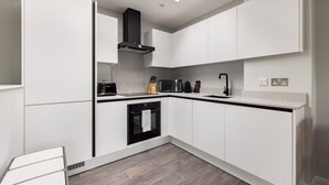 A modern kitchen with white cabinetry, a black range hood, a microwave, a toaster, and a sink. - Hausd - Soho (London)