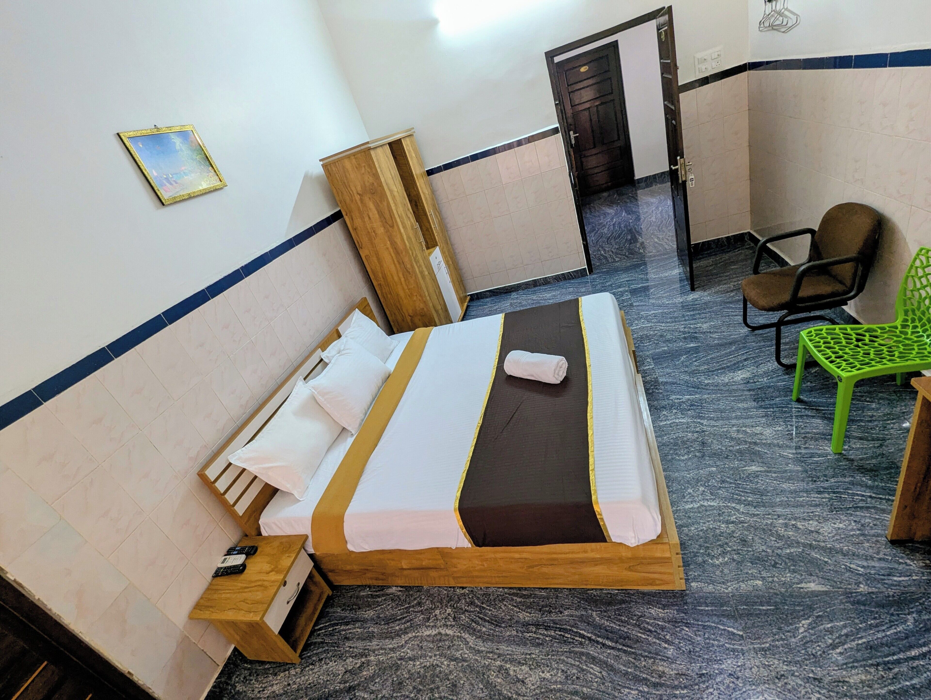 Una habitación de hotel con una cama, una silla verde, un armario de madera y una puerta.