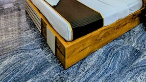 Una camera d'albergo con un letto in legno, una grande finestra con tende, un condizionatore d'aria a parete e un quadro incorniciato appeso al muro.