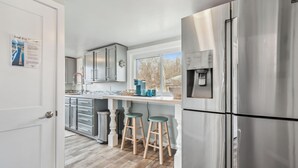 Une cuisine moderne dotée d’appareils électroménagers en acier inoxydable, de tabourets en bois et d’une fenêtre offrant une vue sur l’extérieur.