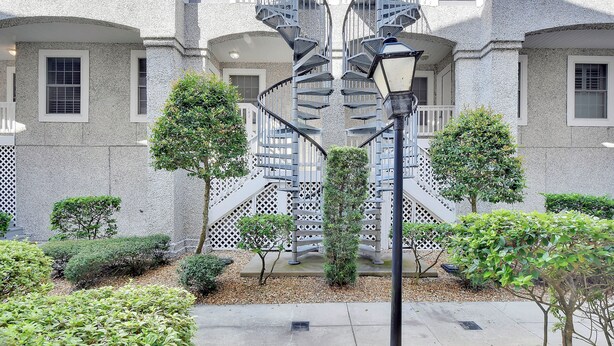 A building with a central spiral staircase, surrounded by greenery and a paved area.