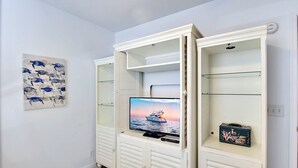 A white entertainment unit with a flat-screen TV, a small decorative box, and a wall-mounted picture of fish.