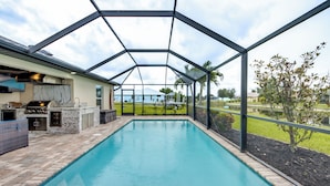 A swimming pool with a covered patio area, a barbecue grill, and a view of a house and landscape. - 4 Bedroom Fresh Water Canal Home with Saltwater Pool and Hot Tub! (Cape Coral, FL)