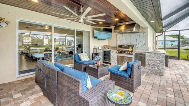 An outdoor patio with wicker furniture, a ceiling fan, and a stone barbecue area. - 4 Bedroom Fresh Water Canal Home with Saltwater Pool and Hot Tub! (Cape Coral, FL)