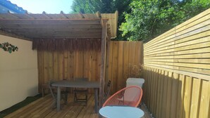 A wooden deck with a table and two chairs, surrounded by a wooden fence and a covered area with a thatched roof. - L'Appartement Myrade, pretty T2 on the edge of the forest (Biscarrosse)