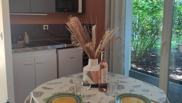 A dining area with a table set for two, a vase with dried plants, and a bottle of wine. - L'Appartement Myrade, pretty T2 on the edge of the forest (Biscarrosse)