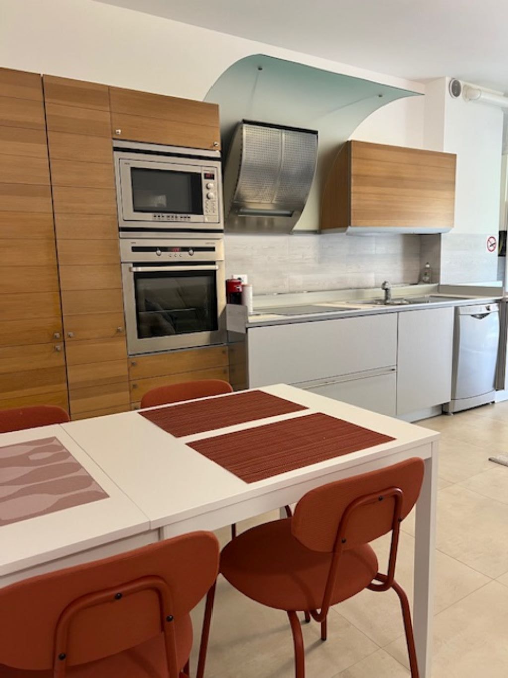 A kitchen with a white countertop, two ovens, a microwave, and wooden cabinets.
