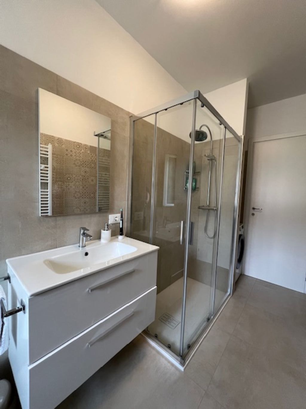 A modern bathroom with a glass-enclosed shower, a white vanity with a sink, and a large mirror.