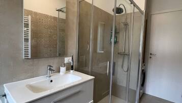 A modern bathroom with a glass-enclosed shower, a white vanity with a sink, and a large mirror.