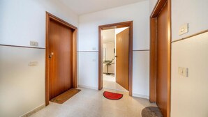 Um corredor com portas de madeira, um tapete de entrada vermelho e chão claro.