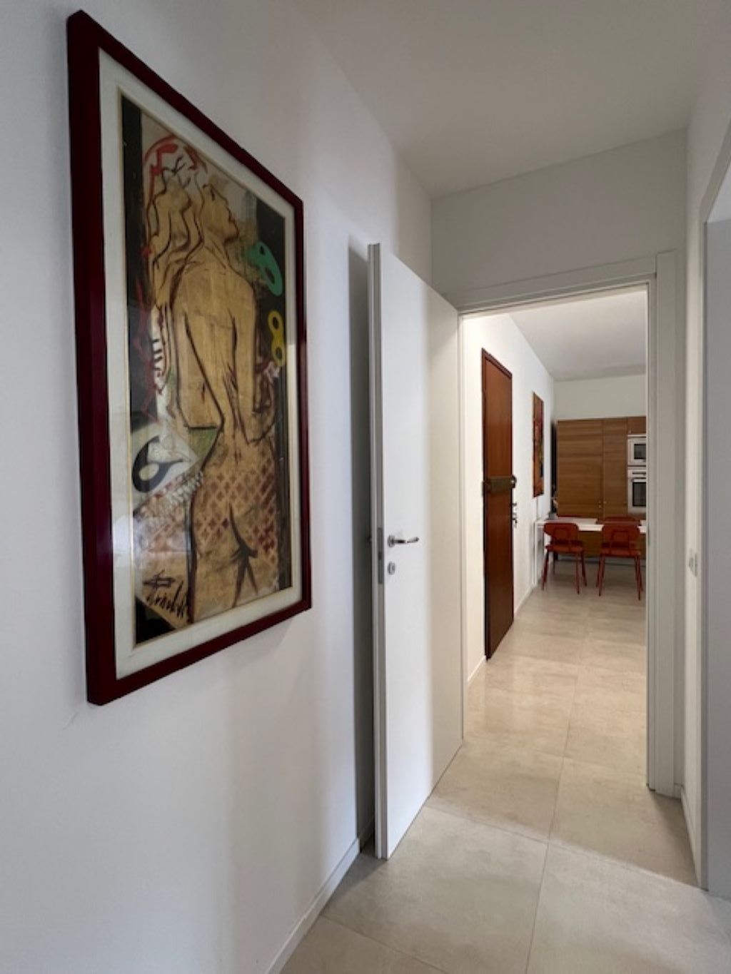 Un pasillo con una obra enmarcada en la pared, que conduce a un comedor con sillas y una mesa.