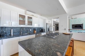 A modern kitchen with white cabinets, a granite countertop, a built-in stove, and a large island. - Luxury Punta Mita Golf Condo – Family Getaway, Private Pools & Beach Clubs (Nayarit)