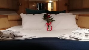 A neatly made bed with white linens, a red rose in a vase, and a tray with a towel and a bottle.