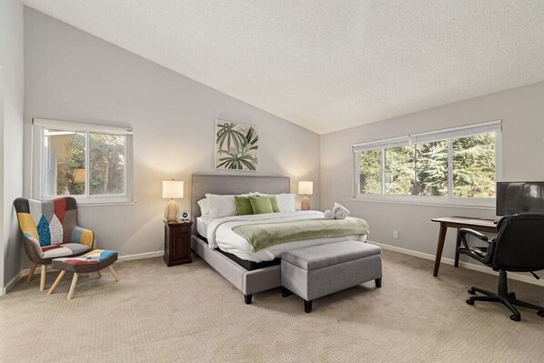 A bedroom with a bed, bedside tables, a chair, a desk, and a TV.