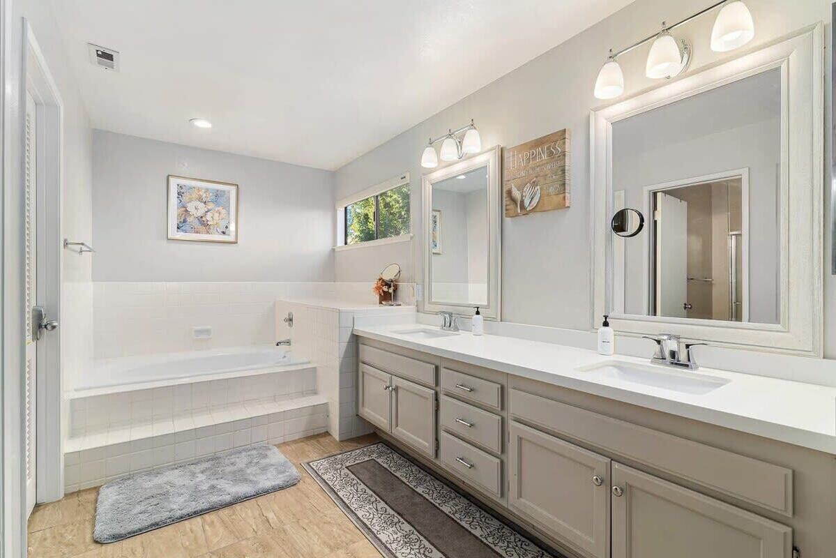 A modern bathroom with a bathtub, two sinks, and a large mirror.