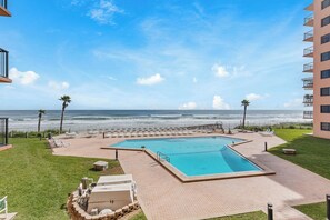 A pool area with a view of the ocean, lounge chairs, and a building with balconies. - ☀️ Oceanfront with Incredible Amenities-Sunrise 206 ☀️ (New Smyrna Beach)