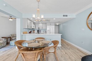 A modern kitchen with white cabinets, a central island, and a dining area with wicker chairs. - ☀️ Oceanfront with Incredible Amenities-Sunrise 206 ☀️ (New Smyrna Beach)