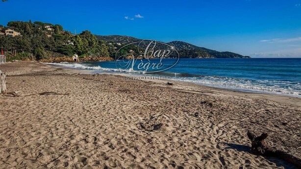 A beach with clear blue water, a sandy shore, and a hill with buildings in the background. - 3-star-rated cottage for 6 people in a residence with a 50-meter pool near Pramousquier Beach (Le Lavandou)