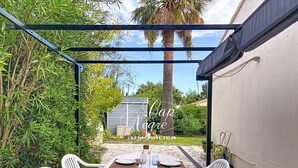A covered outdoor dining area with a table set for four, surrounded by white plastic chairs, under a metal pergola. - 3-star-rated cottage for 6 people in a residence with a 50-meter pool near Pramousquier Beach (Le Lavandou)