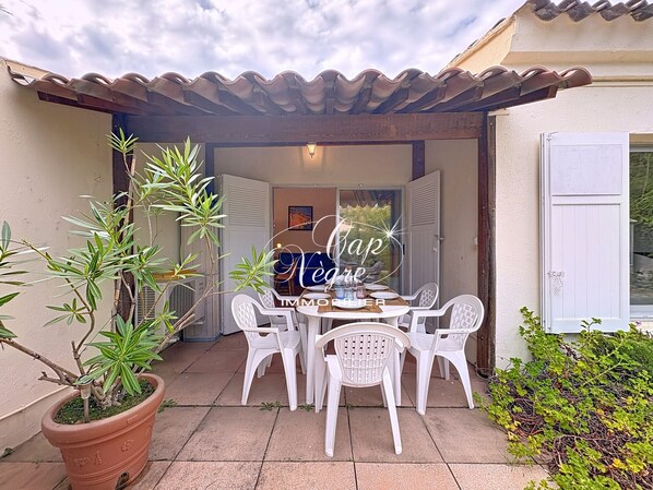 A patio with a table and chairs, a potted plant, and a door with shutters.