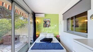 Une petite pièce étroite comprenant un lit, une petite table et une fenêtre.