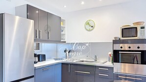 Une cuisine moderne dotée d’appareils électroménagers en acier inoxydable, de meubles gris, d’un évier et d’une horloge murale.