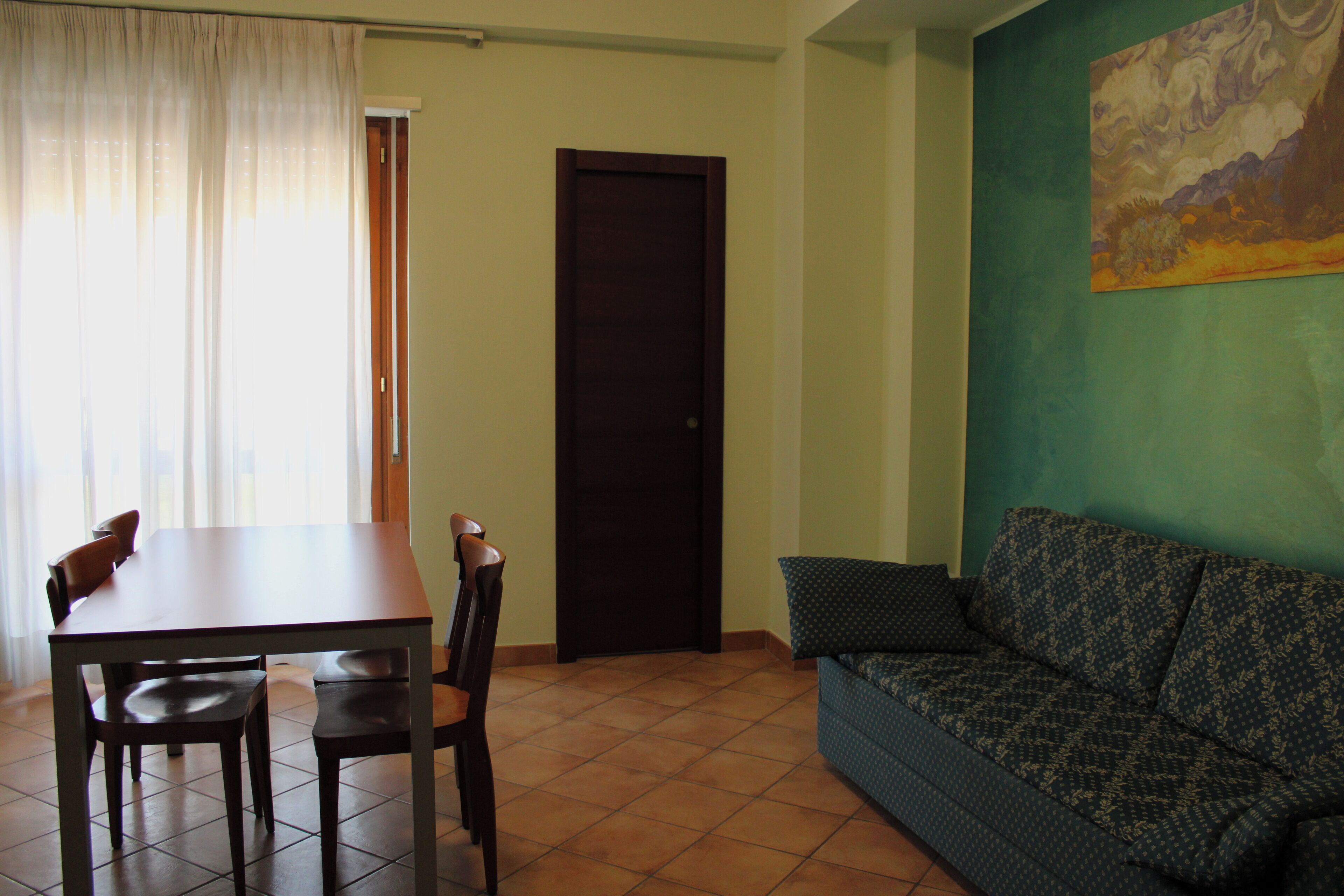 Una habitación con una mesa de comedor, sillas, un sofá, una puerta y un cuadro en la pared.
