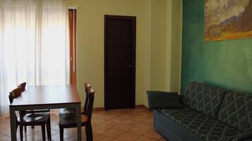 Una habitación con una mesa de comedor, sillas, un sofá, una puerta y un cuadro en la pared.