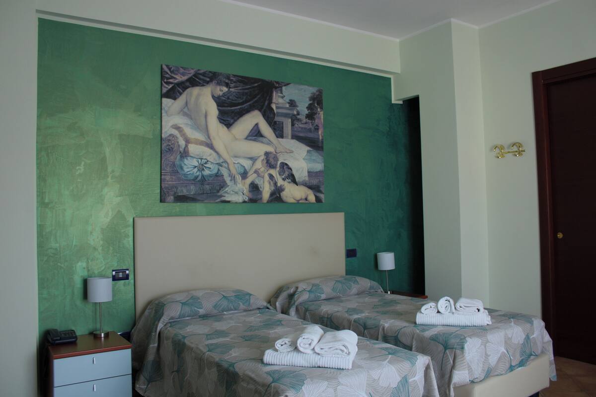 A hotel room with two beds, a painting on the wall, and a door with a brass handle.