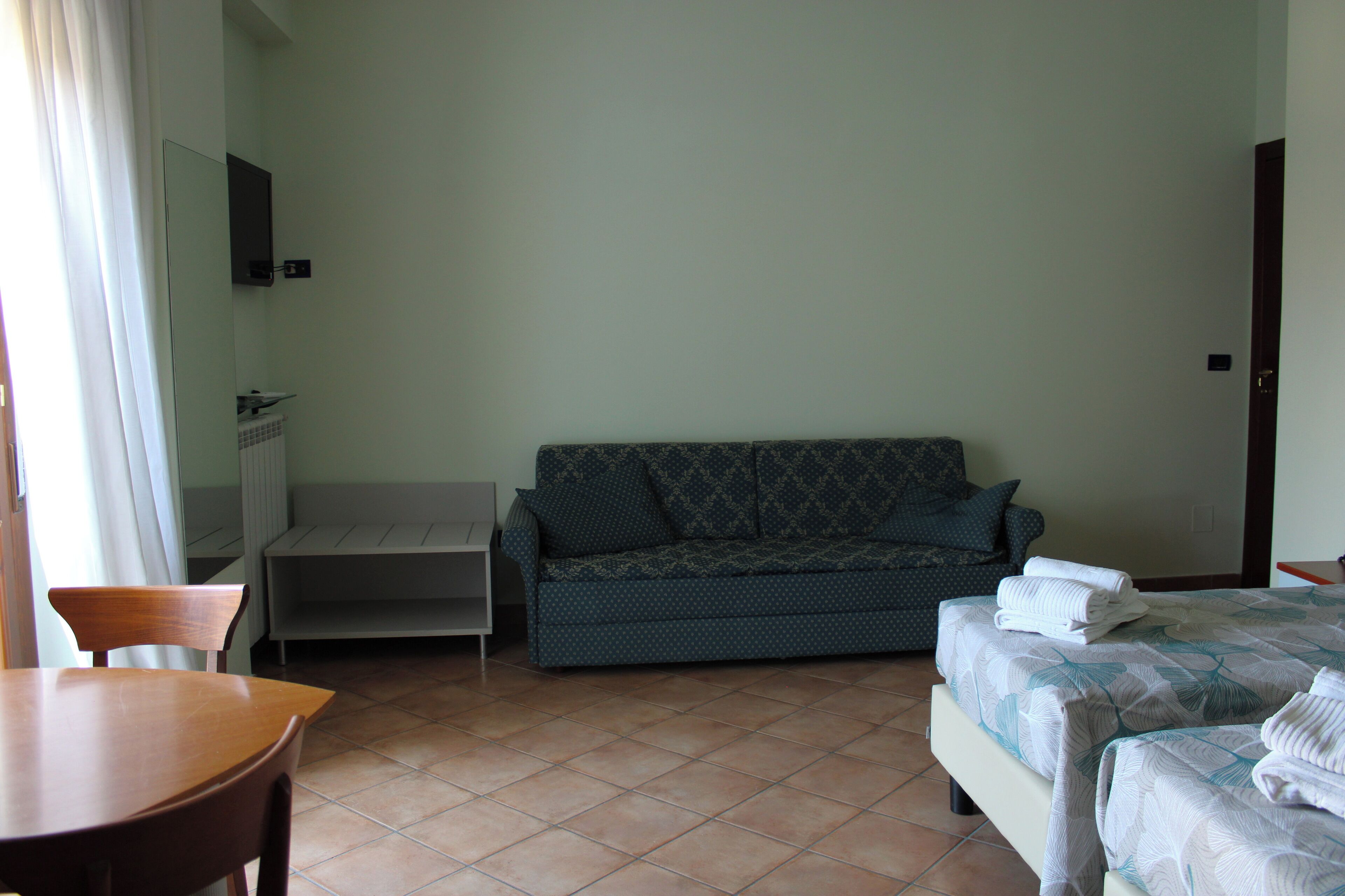 Een kamer met een bed, een slaapbank, een stoel, een tafel en een spiegel.
