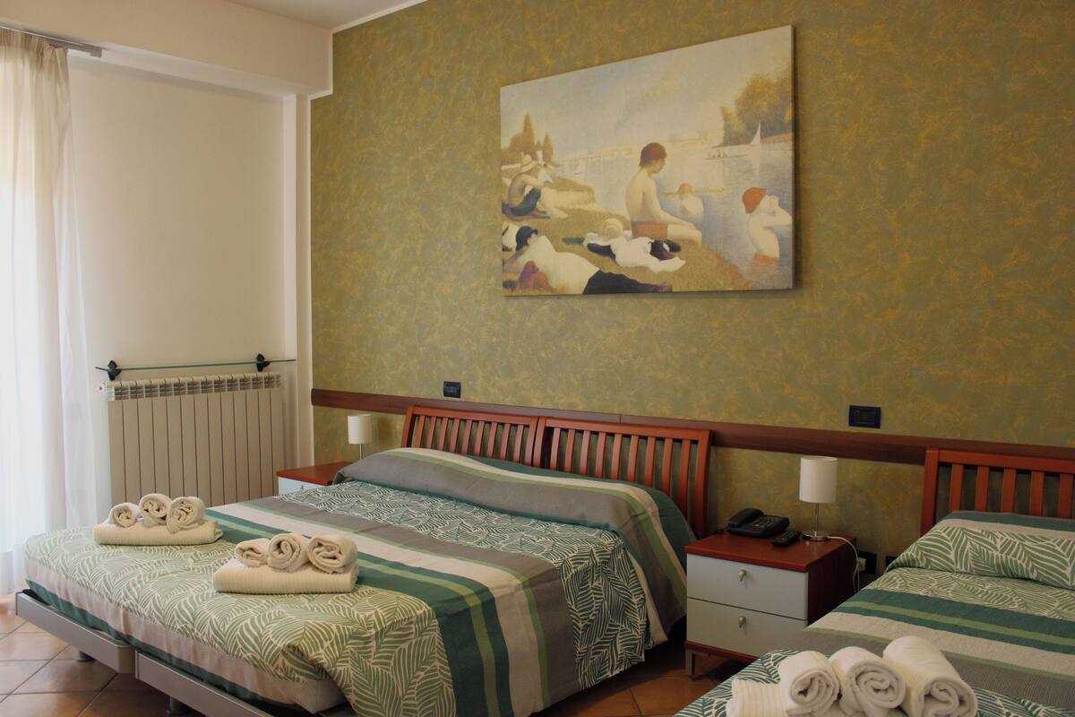 A hotel room with two beds, a painting on the wall, and towels neatly folded on each bed.