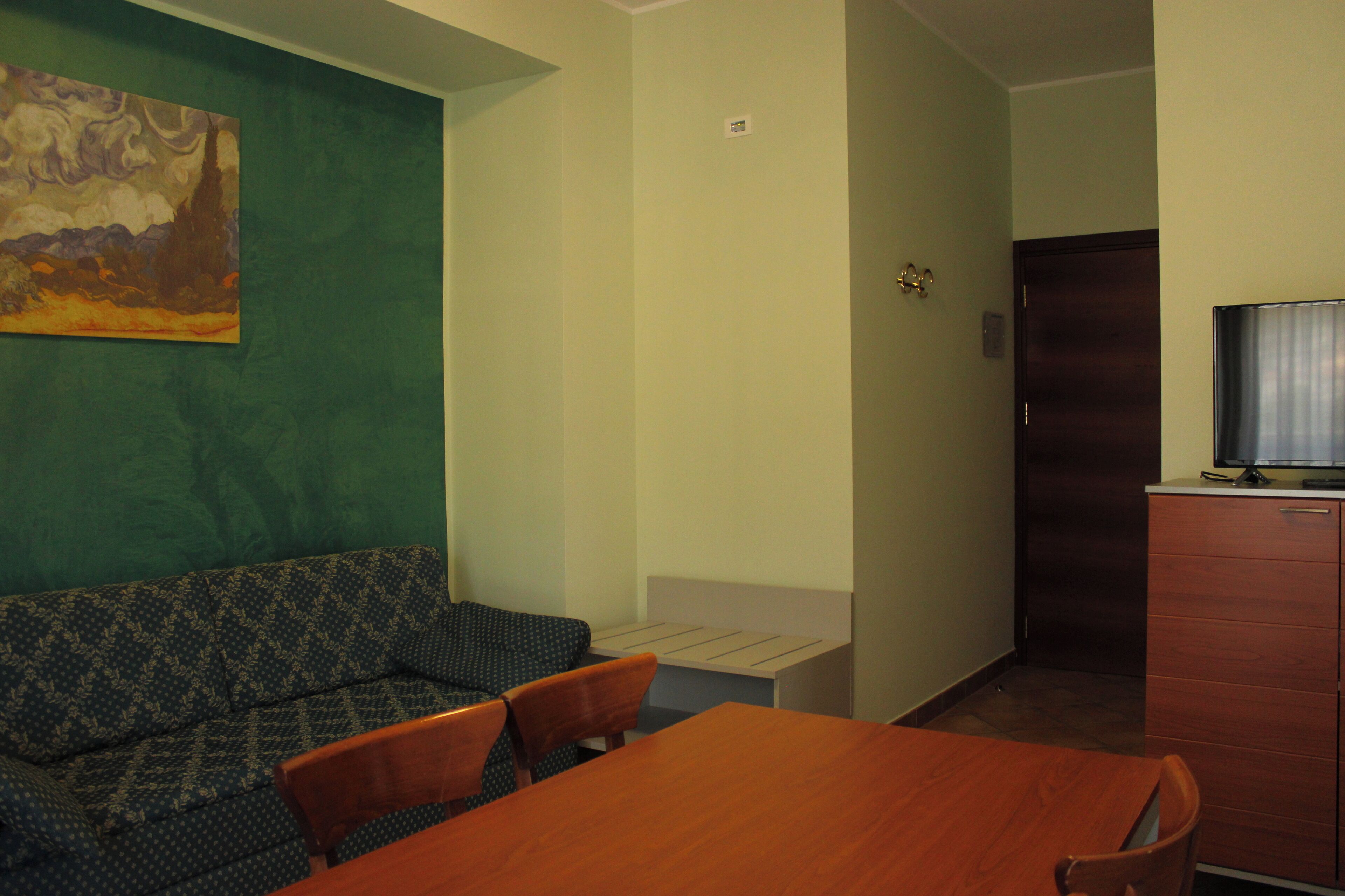 Um quarto com parede verde, um sofá estampado, uma mesa de madeira e uma televisão em um armário.