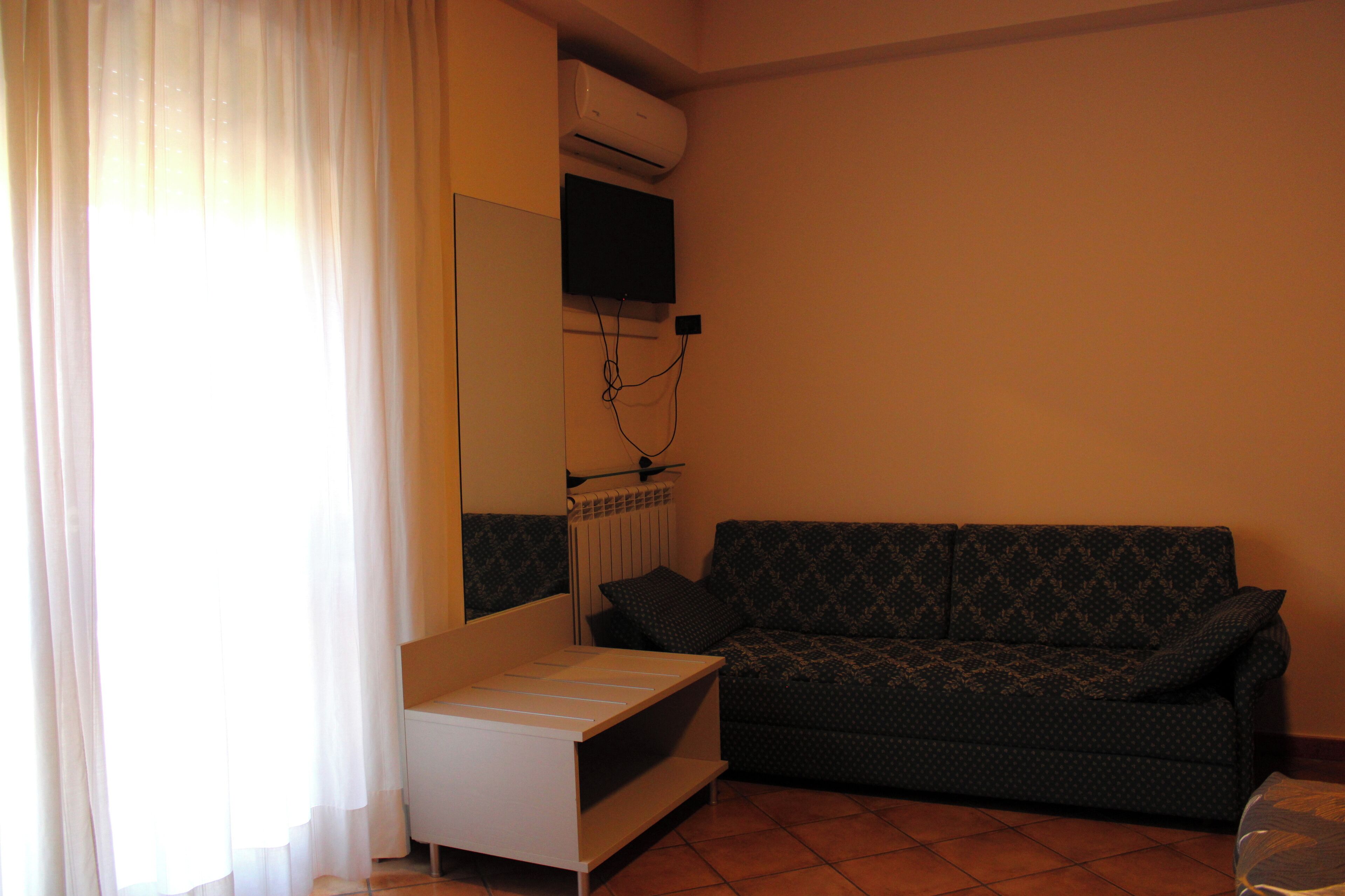 A living room with a sofa, a small white table, a radiator, and a TV mounted on the wall.