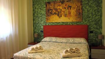 Habitació d'hotel amb un llit, dues nits del taulell i un quadre a la paret, i una finestra amb cortines.
