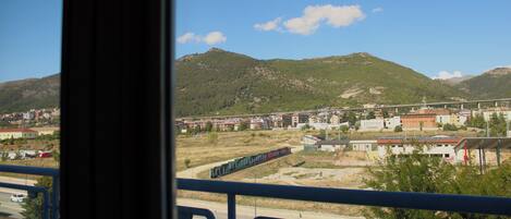 A view from a balcony overlooking a train passing through a town with mountains in the background.
