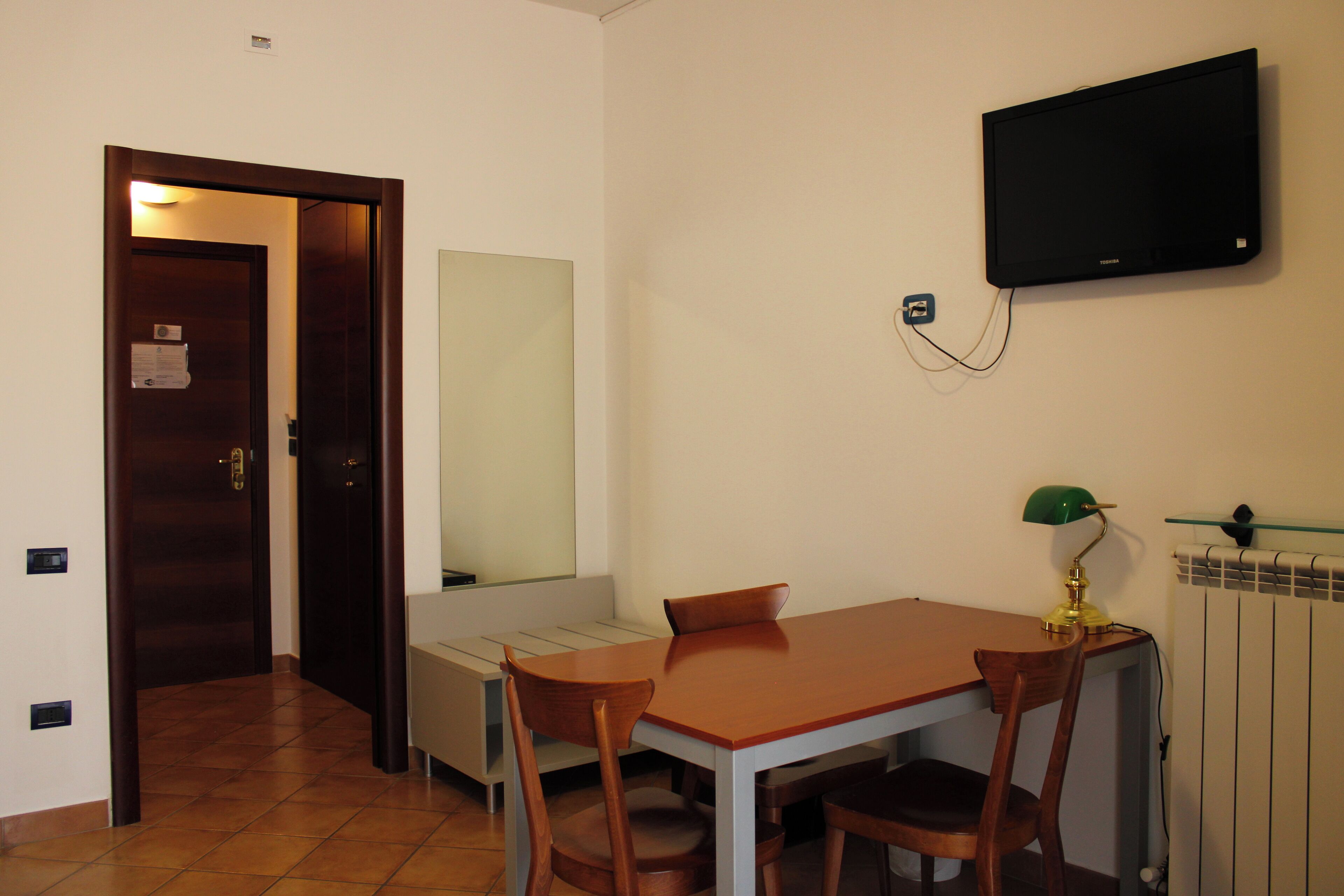 A small dining area with a wooden table and chairs, a television mounted on the wall, and a radiator.